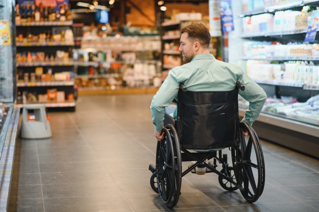 Customer using wheelchair choosing groceries in supermarket